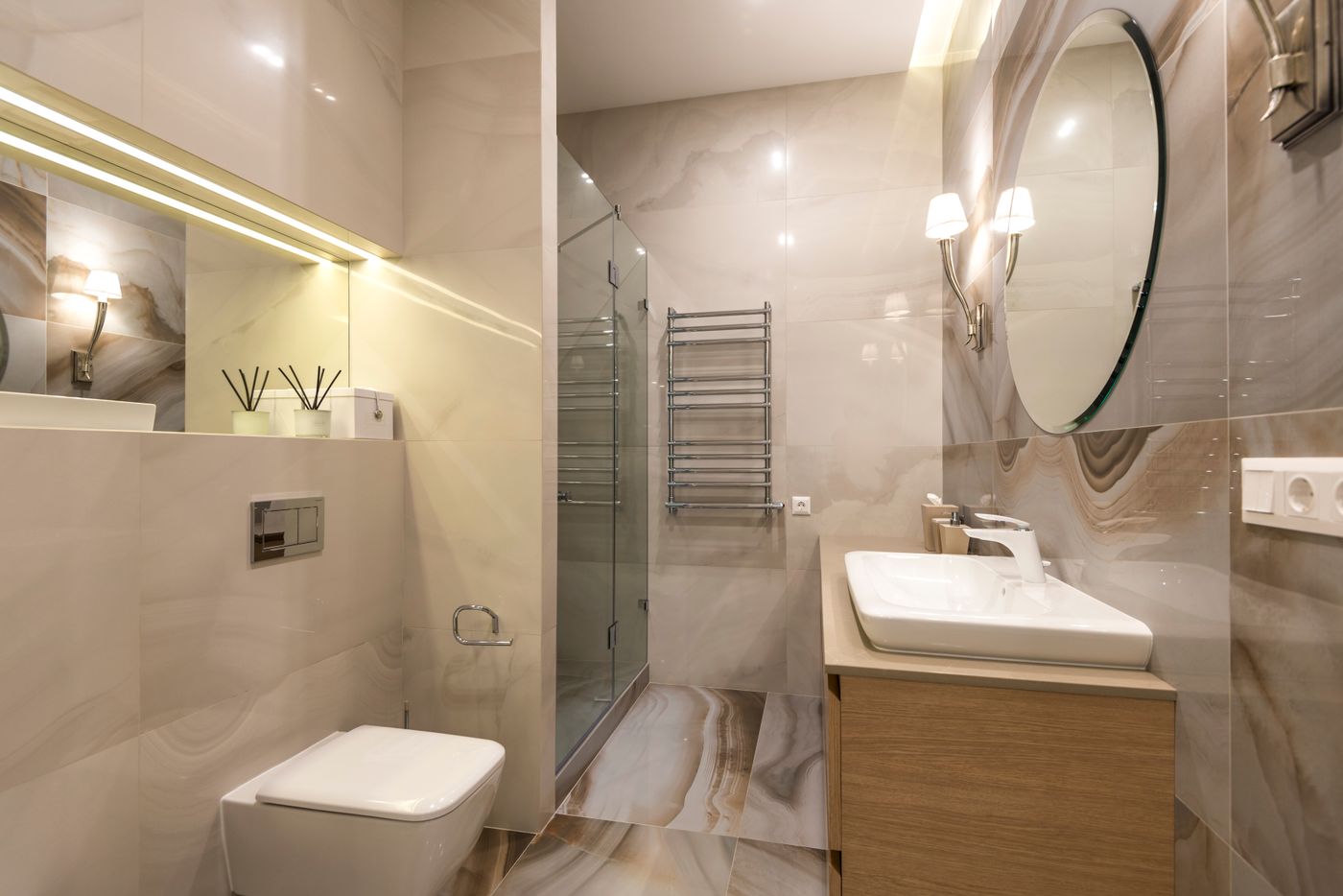 A marble tiled bathroom with a glass shower, heated towel rail and wall hung basin.