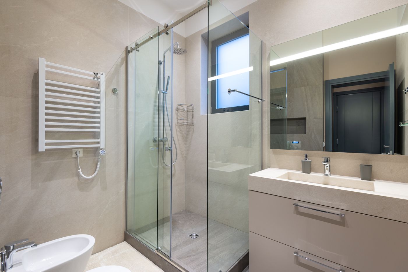 A modern bathroom with a glass shower enclosure, heated towel rail and vanity unit.