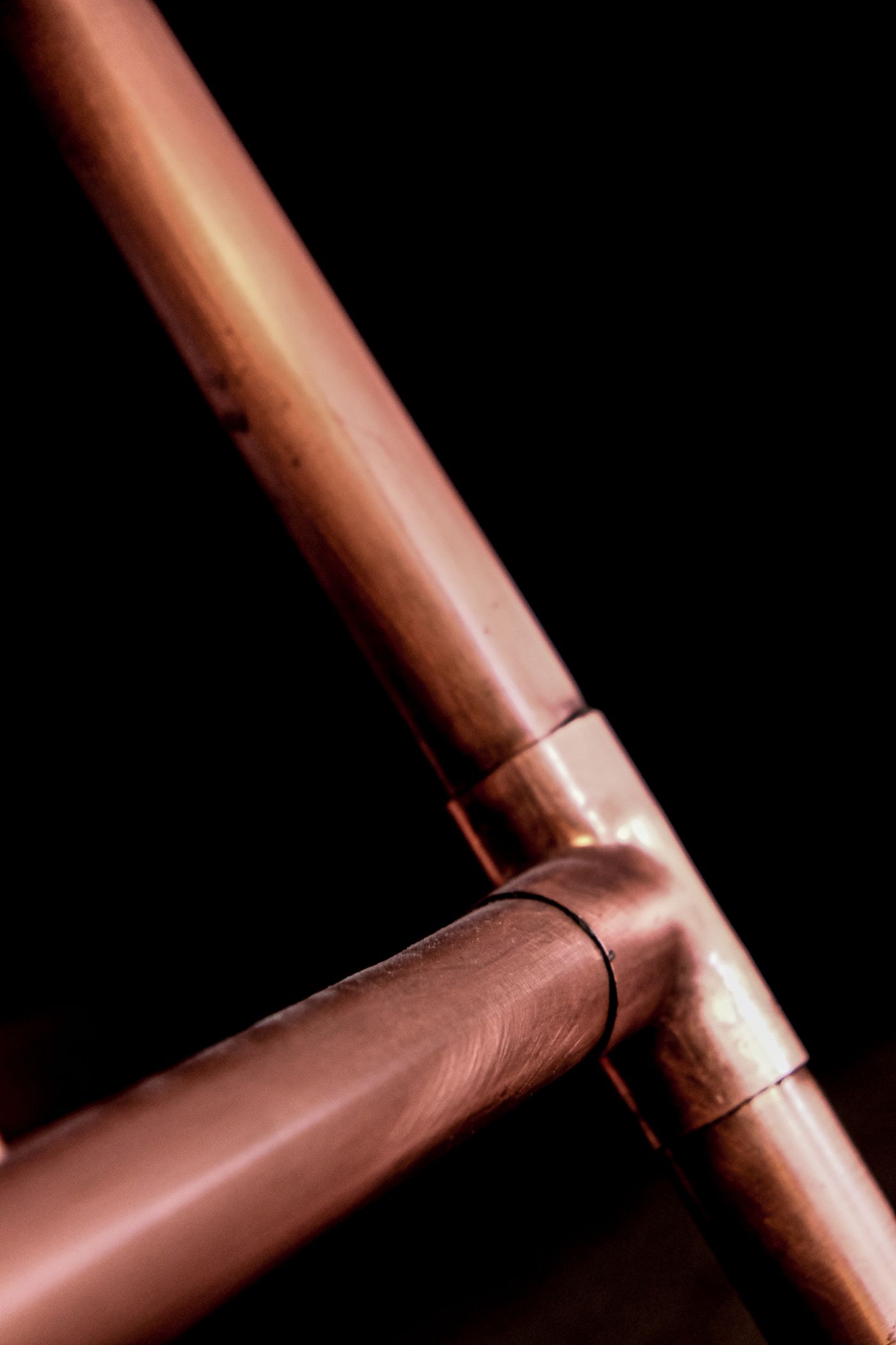 A soldered copper pipe joint photographed against a black background.