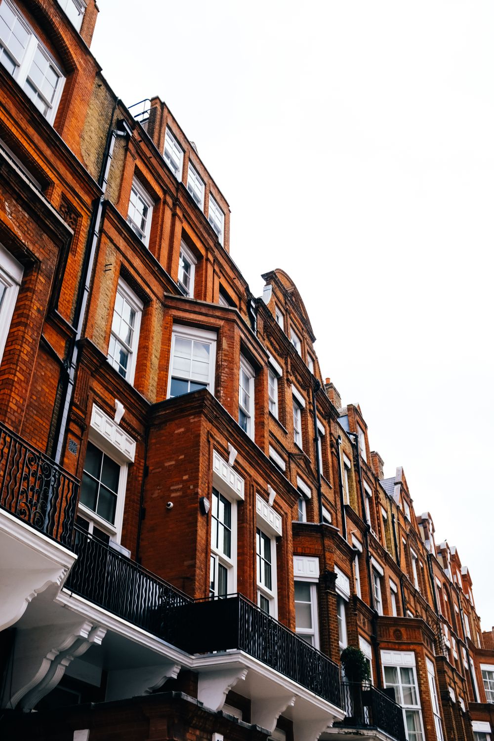 A row of London brick terraced houses with sash windows and iron balconies.