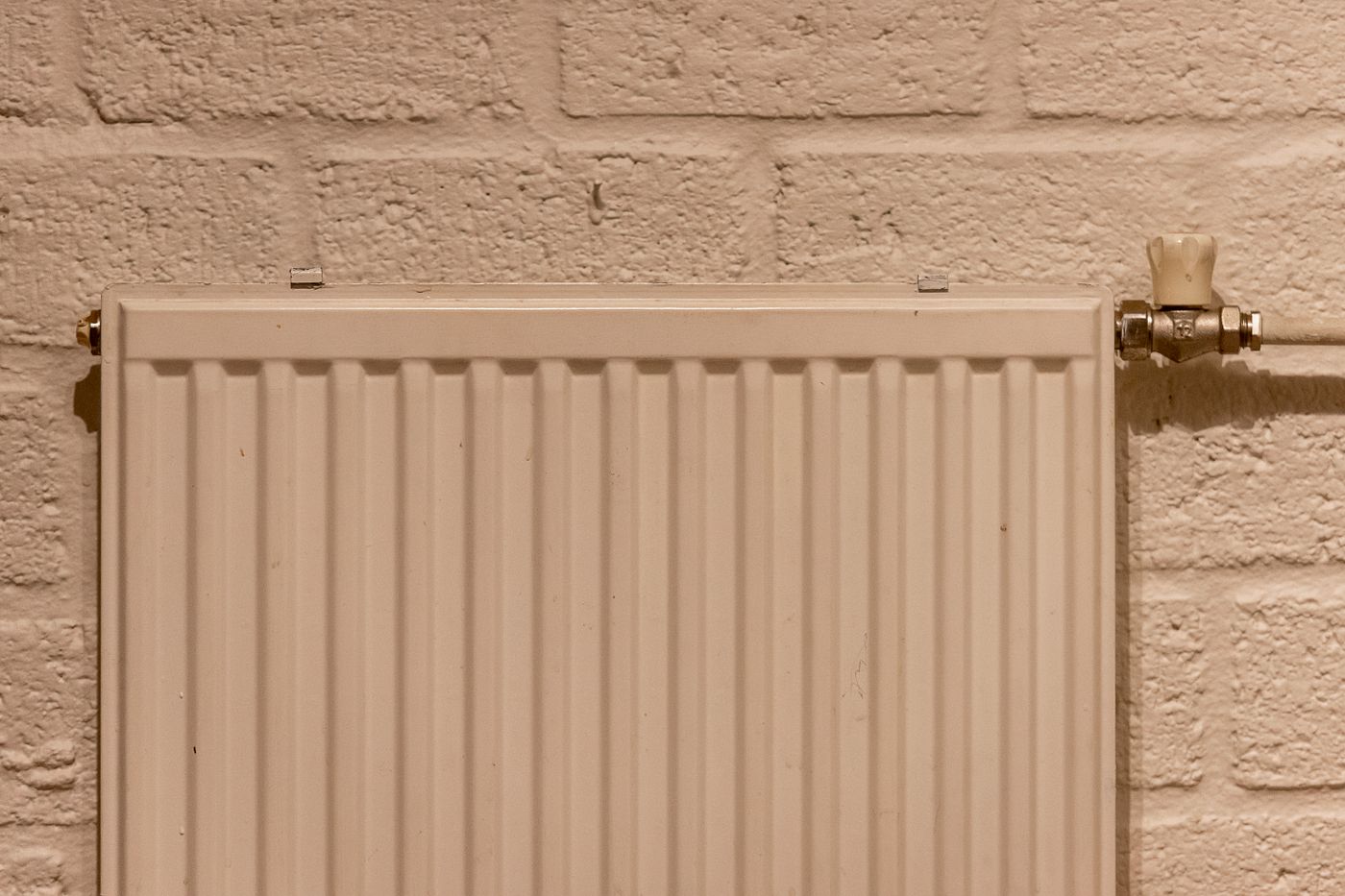 A white panel radiator mounted on a painted brick wall.
