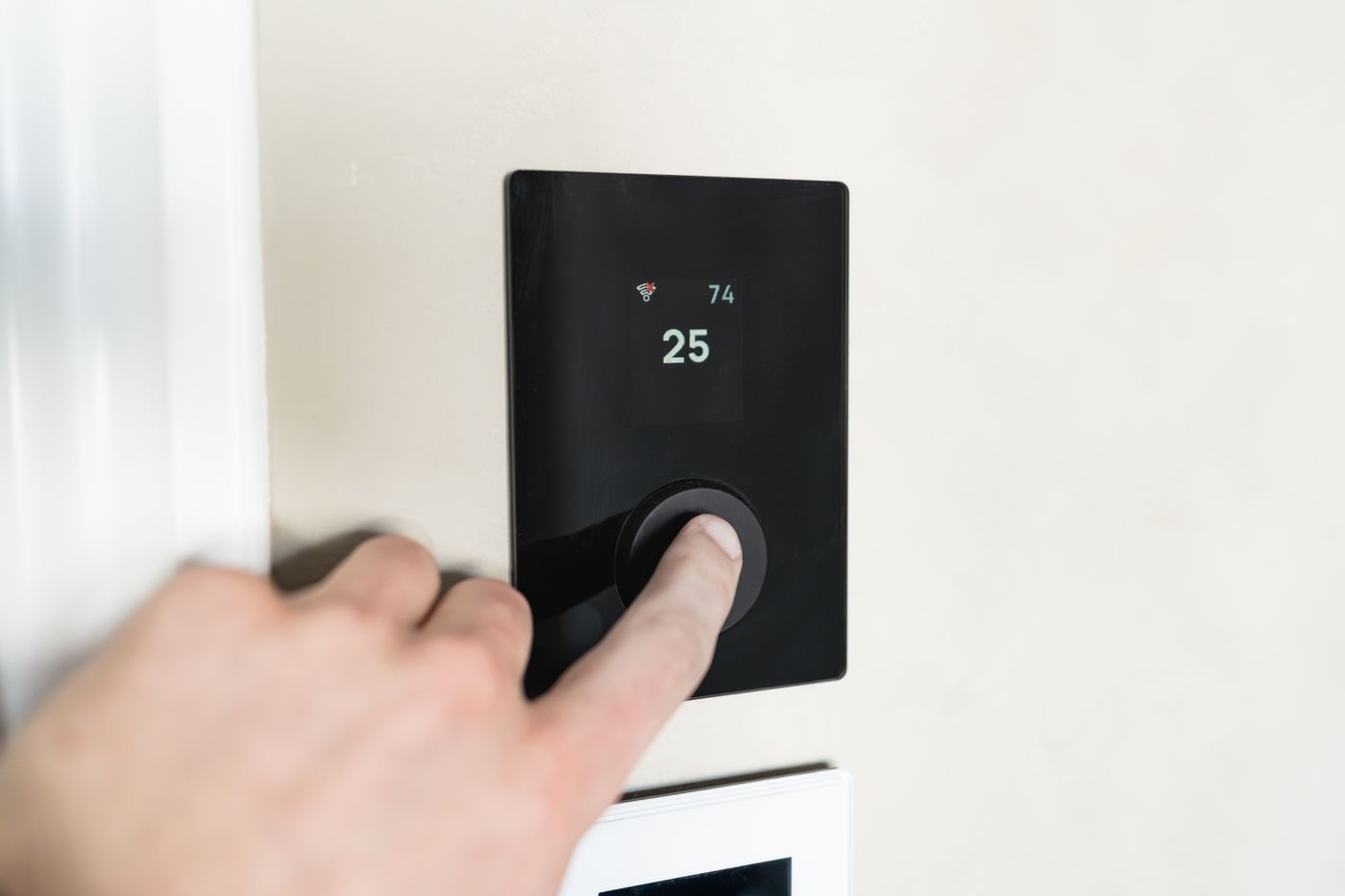 A finger adjusting a wall mounted smart heating control panel.